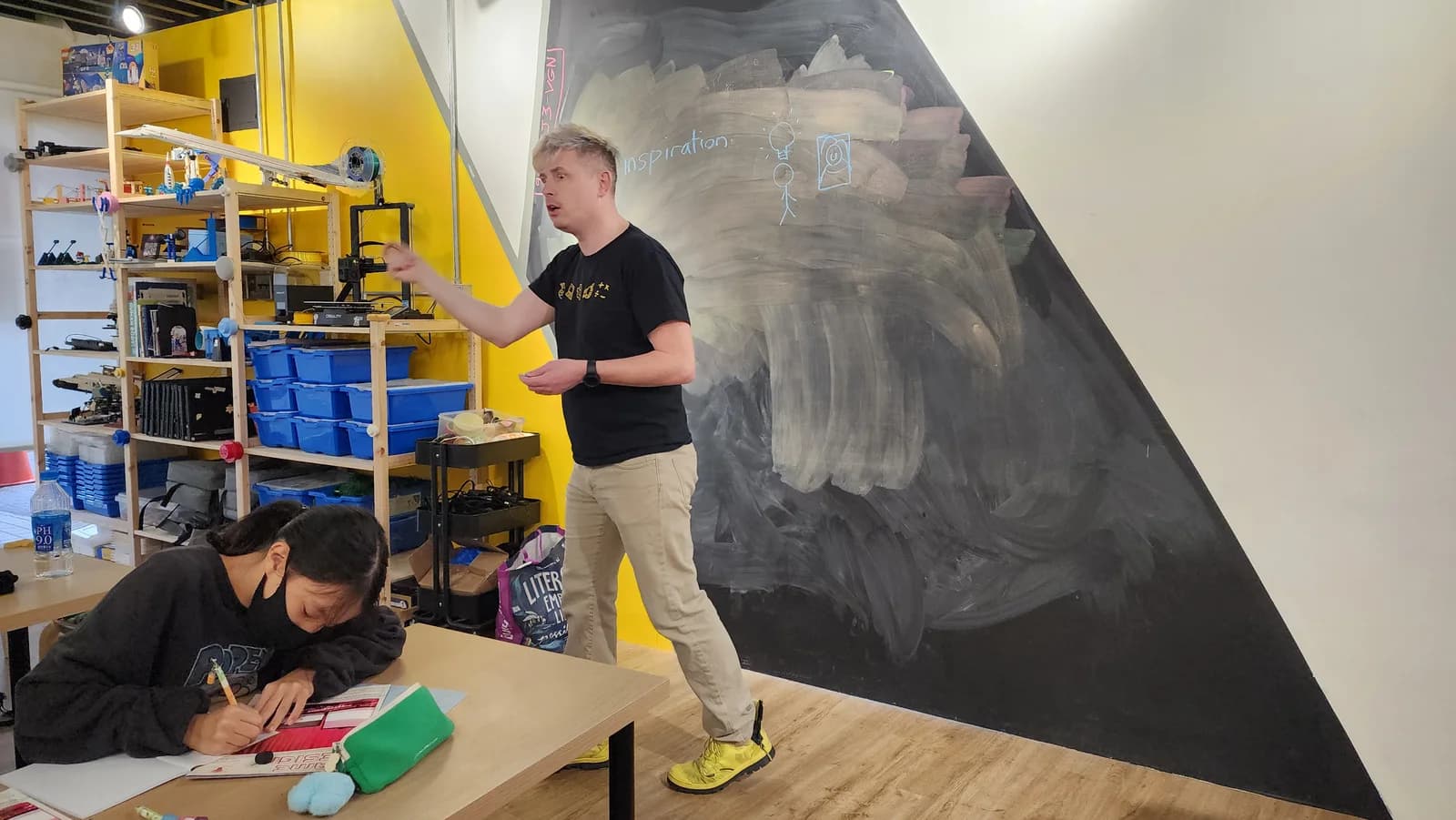 Teacher Paul leads a classroom lesson at the chalkboard while a student takes notes at STEAM SQUAD.