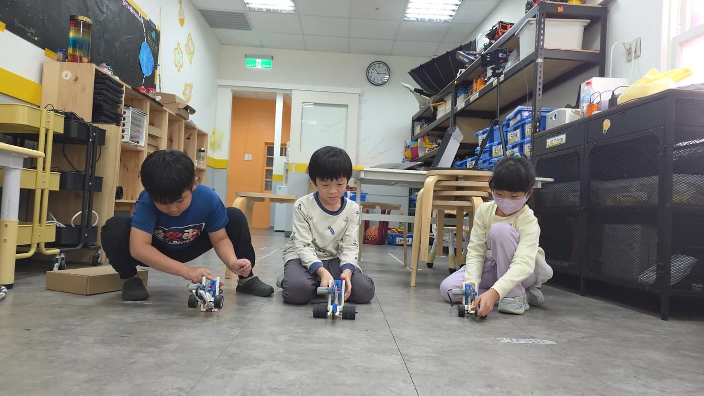Three students testing their mechanisms together on the classroom floor