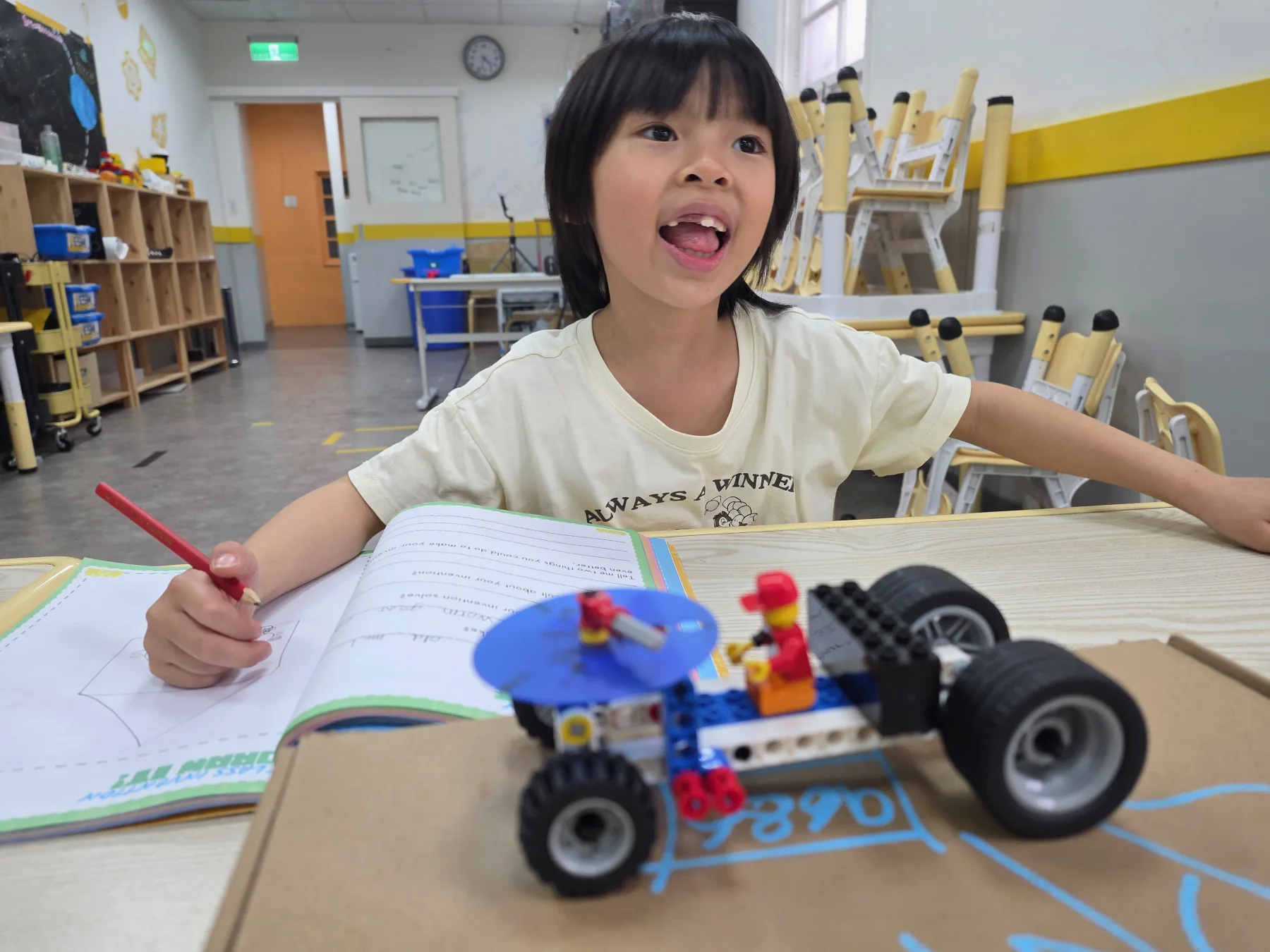 Build Club 學生在課本旁說明由車輪帶動的 LEGO 清掃車