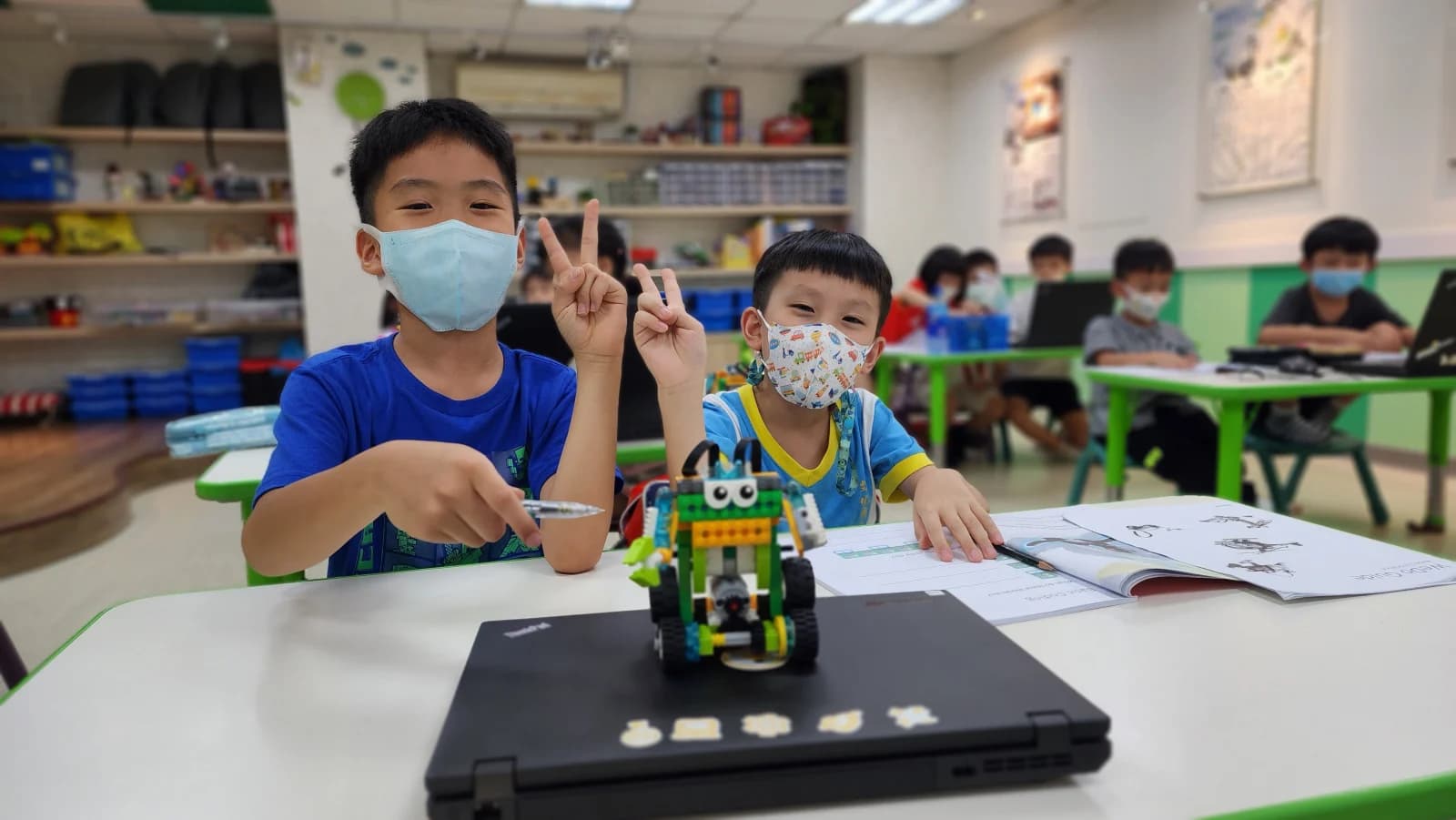兩位學生展示完成的 WeDo 2.0 SmartBot,桌上攤開 CCM 課本