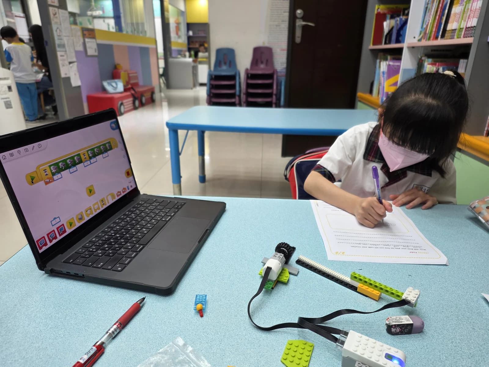 學生在筆電旁記錄 WeDo 2.0 程式測試,桌上有馬達、傾斜感測器與亮燈的 Smart Hub