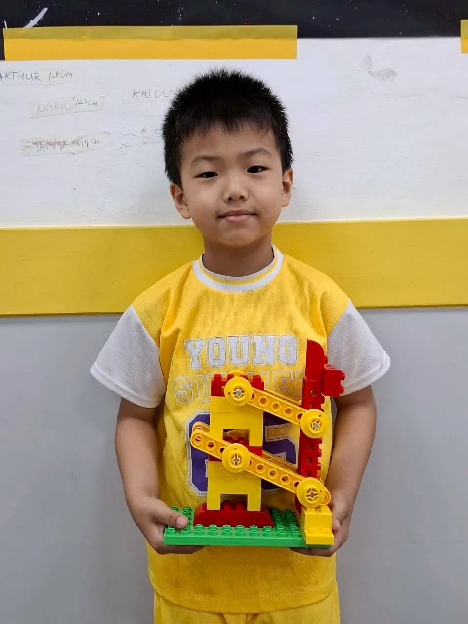 An ESM student holding a tall yellow and red LEGO Giraffe model